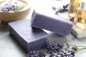 Soap bars, other cosmetic products and lavender flowers on white marble table, closeup