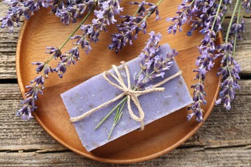 Aromatic soap bar and lavender flowers on wooden table, flat lay