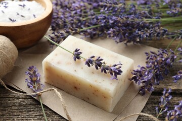 Aromatic soap bar and lavender flowers on wooden table, closeup