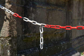 plastic chain with white and red links anchored to a stone wall