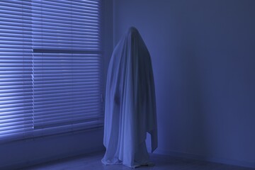 Creepy ghost. Man covered with white sheet indoors in blue light