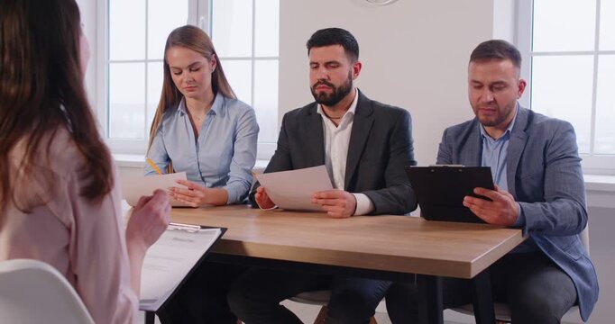 Three professional HR managers sitting in office and listening to female job candidate. Group of interviewers asking questions and evaluating applicant responses and experience during job interview.