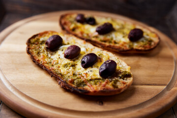 Bruschetta with mozzarella and cheddar cheese, olive pesto and kalamata olives. on wooden background. Soft focus. Close up	