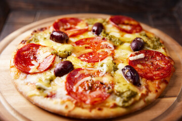 Pizza with chorizo ​​sausage, mozzarella and cheddar cheese, olive pesto and kalamata olives. Wooden background. Soft focus. Close up.	