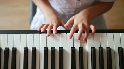 Close-up view of a young girl’s hands playing piano keys at home. Child in a white dress practicing music indoors. Concept of early music education, childhood creativity, and home learning.