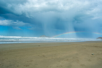 Dramatic Beach Scene with Rainbow and Rain Showers
