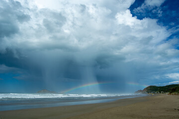 Dramatic Beach Scene with Rainbow and Rainfall