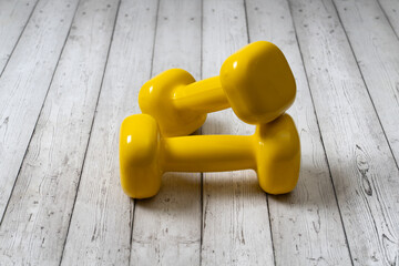 Yellow dumbbells on wooden background. Sports equipment.