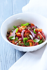 Simple salad with cherry tomatoes, red onion and fresh herbs. Bright wooden background. Close up.	