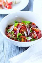 Simple salad with cherry tomatoes, red onion and fresh herbs. Bright wooden background. Close up.	