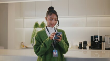Focused highschool student part of diverse team of people at startup office. She shows contentment while connecting on her mobile device in company breakroom