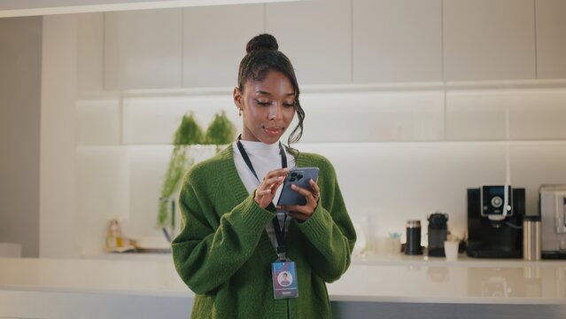 Focused highschool student part of diverse team of people at startup office. She shows contentment while connecting on her mobile device in company breakroom