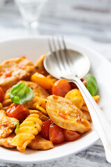 Pasta with chicken breast, cherry tomatoes and fresh basil. Bright wooden background. Close up.