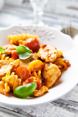 Pasta with chicken breast, cherry tomatoes and fresh basil. Bright wooden background. Close up.