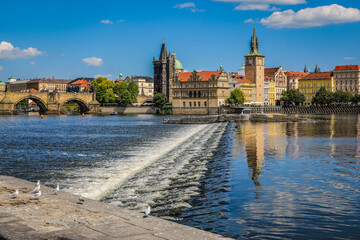 Fototapeta premium Charles Bridge and Old Town buildings in Prague, Czech Republic, with a view of the weir on the Vltava River and seagulls on the riverbank.