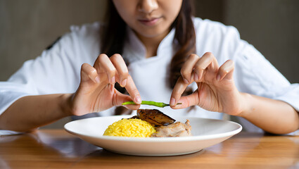 Chef meticulously garnishing gourmet saffron rice dish with chili pepper, close-up.