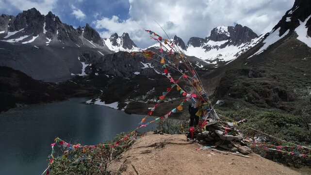Caucasian person standing next to a cairn with prayer flags, overlooking a lake and mountains