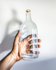 Mockup glass bottle in hand, clear glass bottle, empty, bright background, hand holding