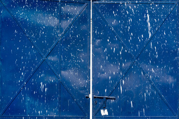 Blue painted metal gate with white paint splatters and weathered surface. Industrial door with...