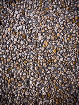 A full frame of small, irregularly shaped pebbles in various shades of brown and grey, embedded in concrete, creating a textured, natural, and rustic surface.