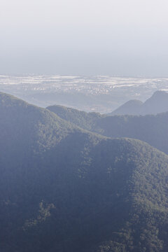 View of verdant mountains receding into a hazy horizon, where the city nestles in the distance, a symphony of blue and green, Avellino, Campania, Italy.