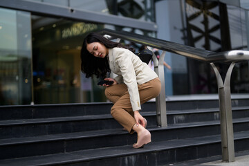 Businesswoman holding her smartphone is having ankle pain on stairs