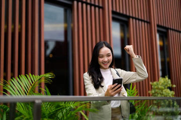 Young asian manager expressing joy and excitement while reading good news on mobile phone