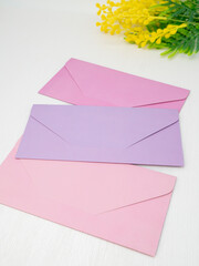 Three pink and lilac closed envelopes for money lie on white background with mimosa flower, holiday message concept