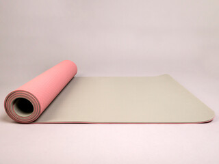 Double-sided pink and gray sports yoga mat in a half-open roll lies on a gray background