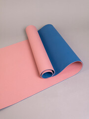 Double-sided pink and blue sports yoga mat in a half-open roll lies on a gray background