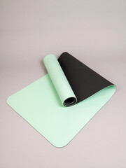 Double-sided light green with black sports yoga mat in a half-open roll lies on a gray background