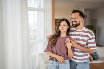 Happy couple embracing and looking out window in new home