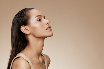 Profile portrait of a young woman with sleek hair, showcasing healthy skin and a serene expression against a warm beige background