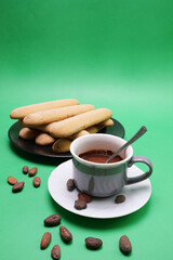 Tazza con cioccolata e piatto con savoiardi sardi per colazione, fave di cioccolata sul tavolo, sfondo verde