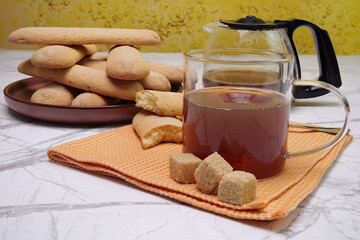 Primo piano di bicchiere con tè, piatto con biscotti e caraffa con tè