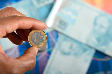 Brazilian real coin held in hand over banknotes