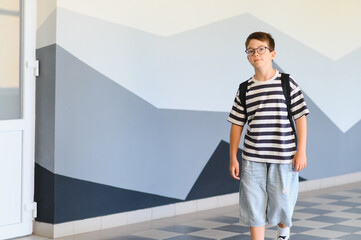 Student walking in school hallway wearing backpack and glasses