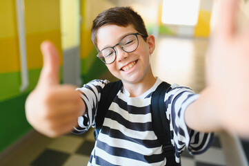 Smiling student giving thumbs up taking selfie in school hallway