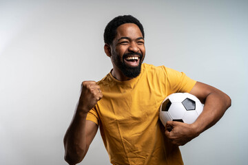 Excited man holding a soccer ball and screaming while showing a win gesture, isolated on gray. © Nenad