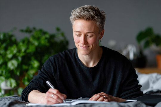 Young woman writing in notebook lying on bed at home - Powered by Adobe