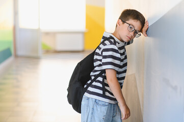 Sad schoolboy crying leaning against wall at school after bullying from classmates
