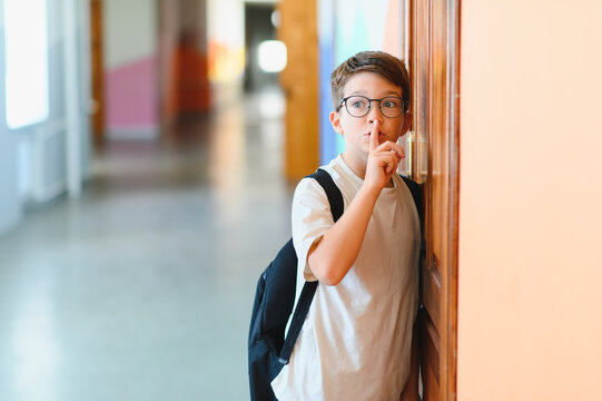 Schoolboy making silence gesture in school hallway - Powered by Adobe