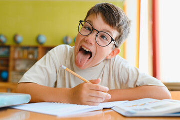 Naughty boy sticking out tongue while studying at school desk