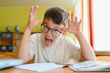 Playful student sticking out tongue in classroom, schoolboy making funny faces