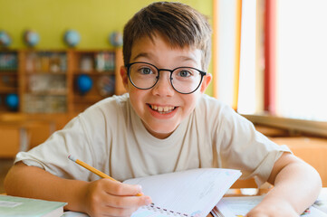 Smiling pupil writing on notebook at school desk
