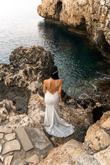 Elegant bridal figure gazes towards tranquil waters in a stunning coastal setting during sunset
