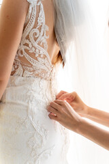 Bridal preparations highlight intricate details as the mother fastens the delicate dress