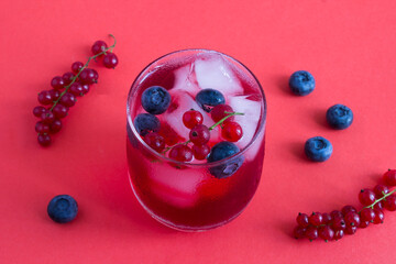 Cold lemonade or cocktail with red currants and blueberry in the drinking glass on a red background. Close-up.