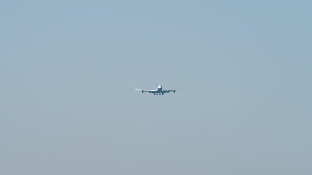 Large aircraft with an unrecognizable livery approaching landing, front view long shot. Airplane in blue sky background. Travel concept