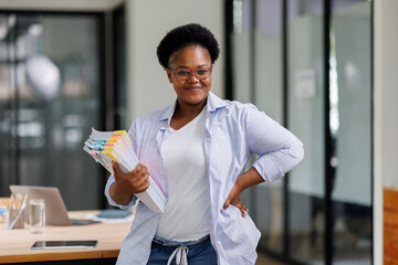 African American organizing documents in hand with colorful clips and sticky notes on desk,...